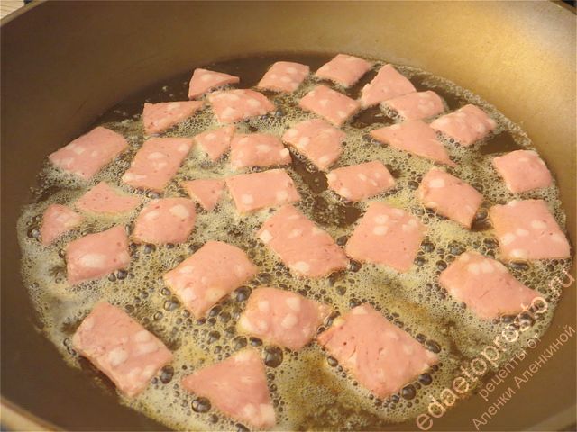 Кладем кусочки колбасы на сковороду обжариваться